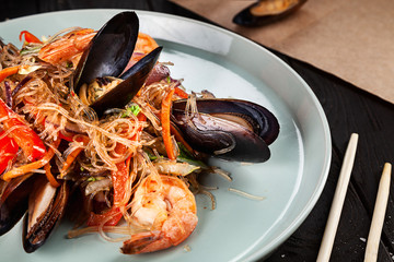 Delicious close up view on Chinese noodles with mussels. Chinese cuisine, dark backround, top view food, copy space for text, selective focus.