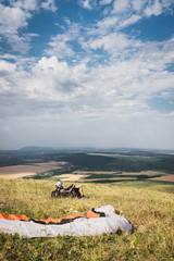A professional paraglider in full gear and a helmet lies and rests on the grass high in the mountains looking at the clouds