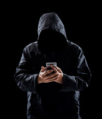 Hacker with hidden face in a hoodie uses a mobile phone to hack the system © showcake