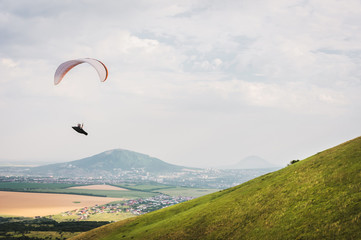 Fototapeta na wymiar A white-orange paraglider flies over the mountainous terrain