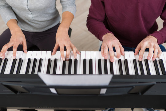 four hands playing on the piano keys