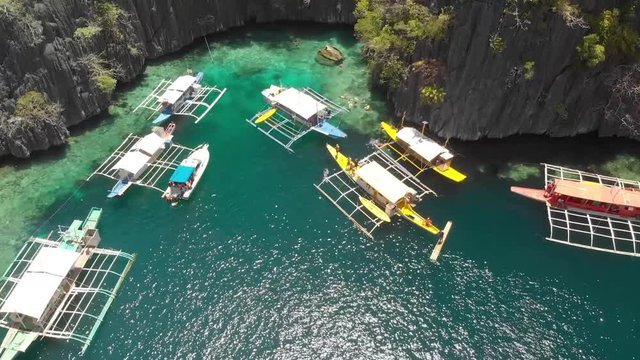 Aerial drone shot of people at Paraw boats, in turquoise lagoons, between limestone cliffs, on a sunny day, at Coron island, Philippines, Asia