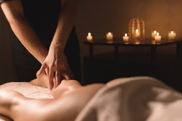 Close-up of male hands doing calf massage of female legs in a dark room with candles in the background. Cosmetology and spa treatments - obrazy, fototapety, plakaty