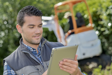 Man looking at tablet, digger working in background
