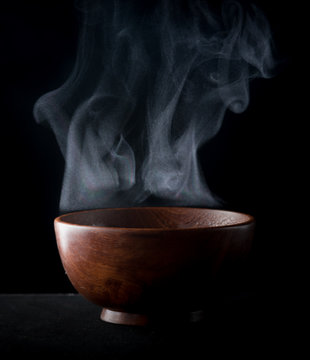 Steam of hot water in a bowl with smoke over dark background