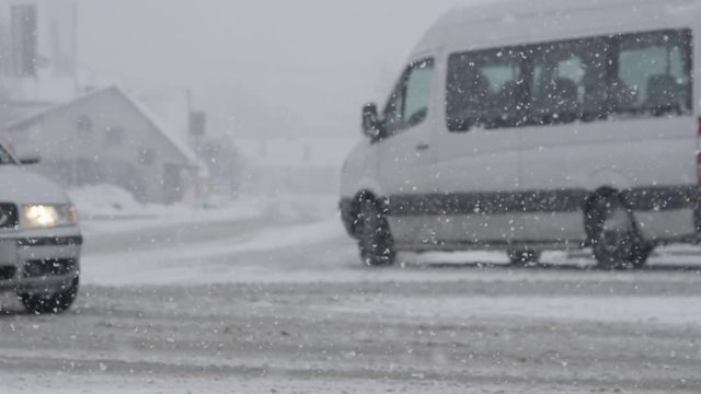 SLOW MOTION, DOF: White van steers into a side street during an intense snowstorm. Idyllic winter weather makes the asphalt road dangerous for the city traffic. Van leaving trails in the dirty snow