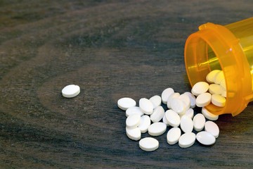 Pile of white pills spilled from a prescription bottle. Concepts of opioid addiction, prescription...