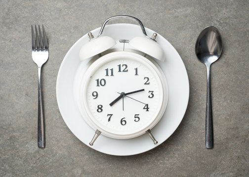 Weight loss or diet concept,Alarm clock on plate with spoon and fork on grey concrete textured