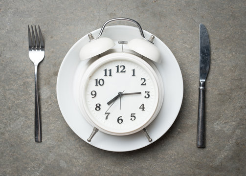 Weight loss or diet concept,Alarm clock on plate with knife and fork on grey concrete textured
