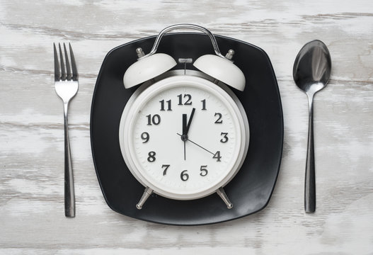 Weight loss or diet concept,Alarm clock on plate with spoon and fork on wood