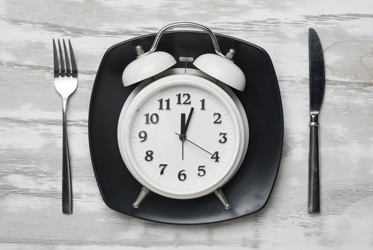 Weight loss or diet concept,Alarm clock on plate with knife and fork on wood