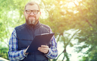 Male ecologist takes notes on the background of green plants.