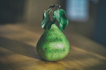 Green pear with leaves on kitchen table - obrazy, fototapety, plakaty