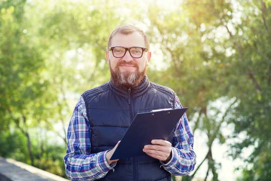 Adult male ecologist with glasses. Man writes information about environmental problems while standing against a background of green plants.