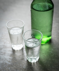Alcoholic clear distilled korean Soju bottle with shot glass on grey concrete textured