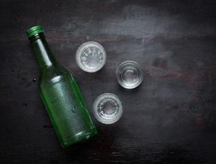 Alcoholic clear distilled korean Soju bottle with shot glass on a wooden background.
