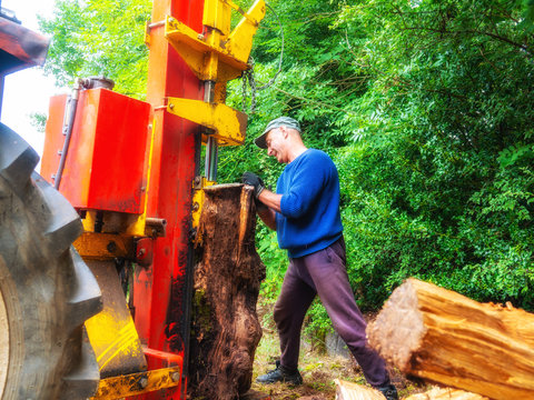 worker splitting logs with power splitter on the back of tractor