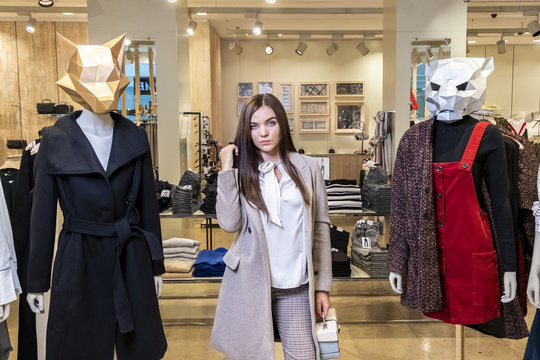 The concept of shopping and fashion. Beautiful serious young brunette girl in a clothing store near mannequins with animal masks.