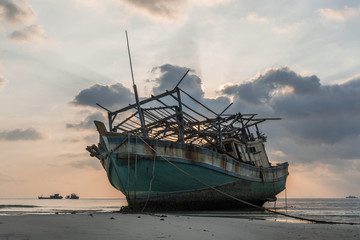 The old wooden ruined fishing boat set aground on the beach at Sunset time