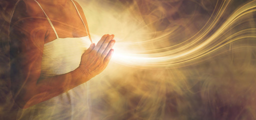 Peaceful prayer sending love and light out -  female in white dress with hands in prayer position and a stream or white light flowing outwards with a rustic golden brown ethereal energy background - obrazy, fototapety, plakaty