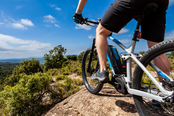 Close up of cyclist on ebike from the lower rear left, landscape and mountains in the background