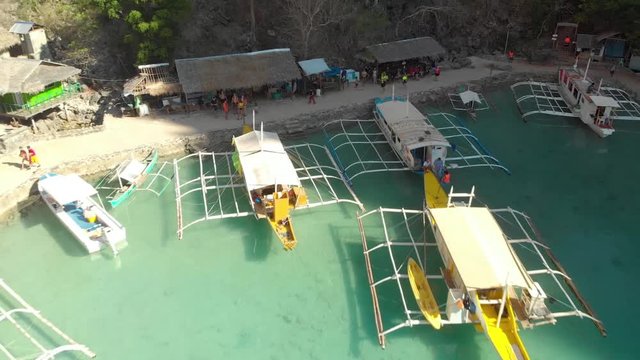 Aerial rising drone shot from people standing at a Paraw boat harbor, in a turquoise lagoon, between limestone cliffs, on a sunny day, at Coron island, Philippines, Asia