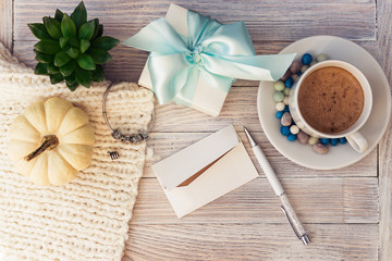 A cup of coffee and colored candies, jewelry boxes, a bracelet with silver charms, succulent and a white decorative pumpkin. Holiday gift with a note.