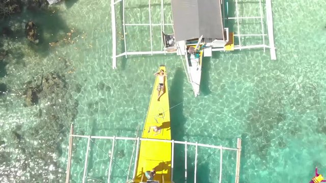 Aerial rising drone shot of a man laying on a Paraw boat, in a turquoise lagoon, in between limestone cliffs, on a sunny day, at Coron island, Philippines, Asia