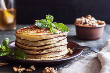 On the table there is a dish with pancakes, honey and nuts.