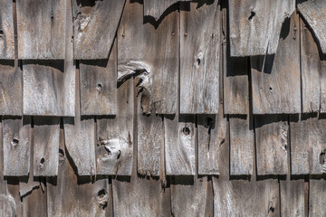 Wooden shake shingles are on the side of a building. The wood is old and graying. Some shingles are broken.