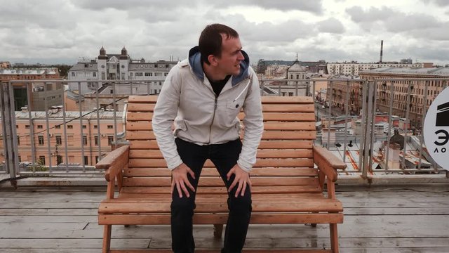 Frozen man in white jacket. Sit down on bench. Feel cold on the roof in the wind