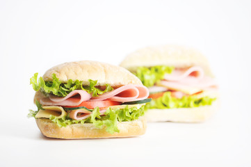 Two sandwiches on a white background. At the heart of the mini ciabatta sandwich. A filling of slices of ham, cheese, lettuce, fresh cucumbers and tomatoes. Close-up.