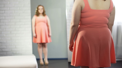Plump girl looking in mirror, dissatisfied with her plus-size appearance
