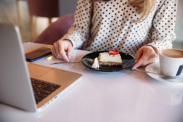 Obraz na płótnie Canvas Girl eating cake in a cafe. Blonde in polka-dot shirt with laptop