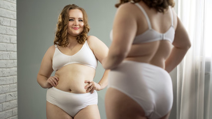 Body positive plump girl looking in mirror, admiring her appearance, femininity