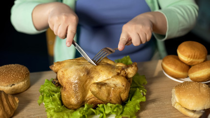 Overweight lady carving roughly roast chicken with fork and knife unhealthy food