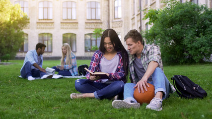 Student couple sitting on lawn on campus, studying, preparing for final test