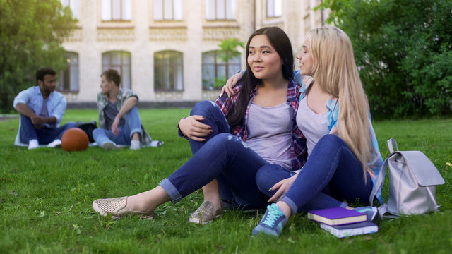 Best friends sitting on lawn near college, hugging, support and friendship