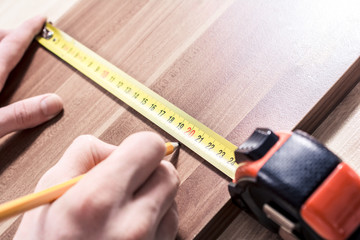 Male Hand Making A Mark At The Measuring Point Of A Measuring Tape On A Brown Wooden Board
