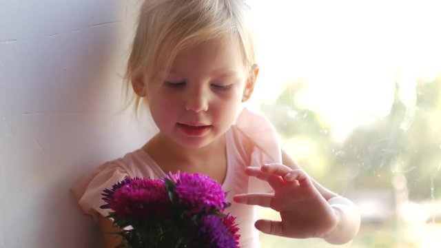 The young ballerina sits on the window and holds flowers in her hands