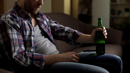 Grubby lonely male on sofa, drinking beer, thinking about problems, depression