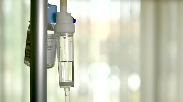 Close up of an antibiotic solution dripping slowly through a medical patient iv into a picc line during a post surgery checkup in a hospital.