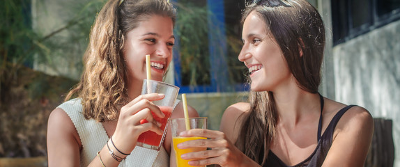 Two girlfriends drinking fruit cocktail on a tropical beach