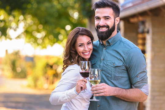 Portrait of young smiling man and woman tasting wine at winery vineyard - Young people enjoying harvest time together. Romantic love.