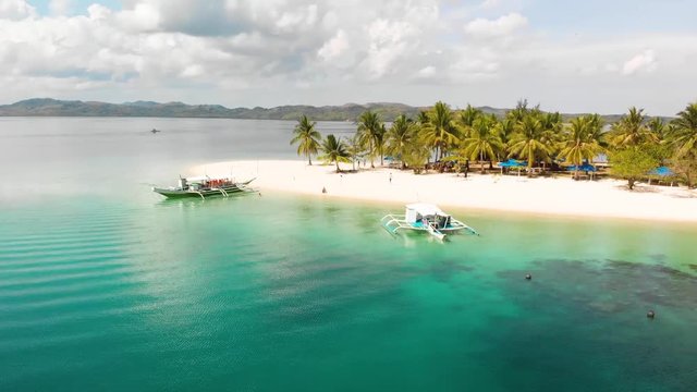 Aerial drone shot towards Paraw boats, in turquoise sea, anchored at a beautiful, tropical isle, at Pass island, in Philippines, Asia