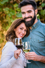 Portrait of young smiling man and woman tasting wine at winery vineyard - Young people enjoying harvest time together. Romantic love.