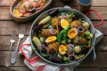 Homemade Hasselback Potatoes in a pat with root vegetables.