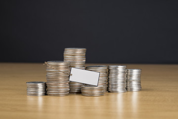 Stacked US quarter coins on wooden table with blank tag label on black background. (For add texts...