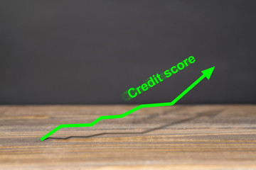 Green upward trend graph shows excellent credit score on wooden surface with black background. Business and financial concept.
