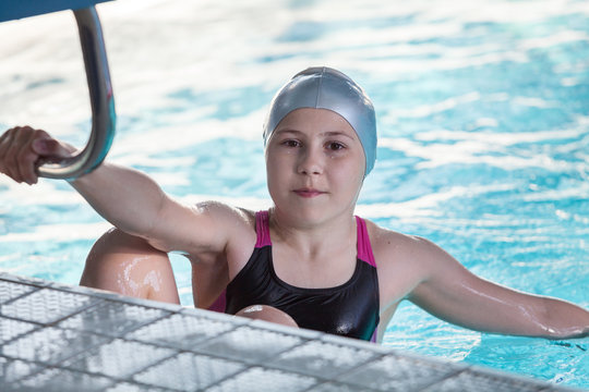 Young girl swimmer, portrait in grey cap at swimming pool